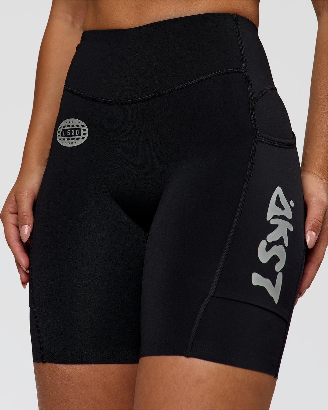 Woman wearing Elite Hype Reflective Run High-Rise 7" Short Pockets - Black-Hype Reflective | Model:Sophia | Size:S - view 1