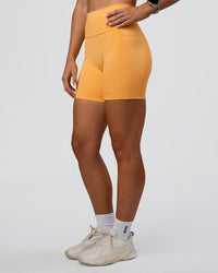 Woman wearing Fusion Ultra High-Rise 6" Short Pockets - Warm Apricot | Set:true | Angle:side | Model:Emelia | Size:S | Thumbnail Index: 6