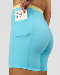 Woman wearing Lume Fusion Mid-Rise V Contour 6" Short Pockets - Baltic Sea-Lemon | Model:Grace | Size:XS | Thumbnail Index: 2