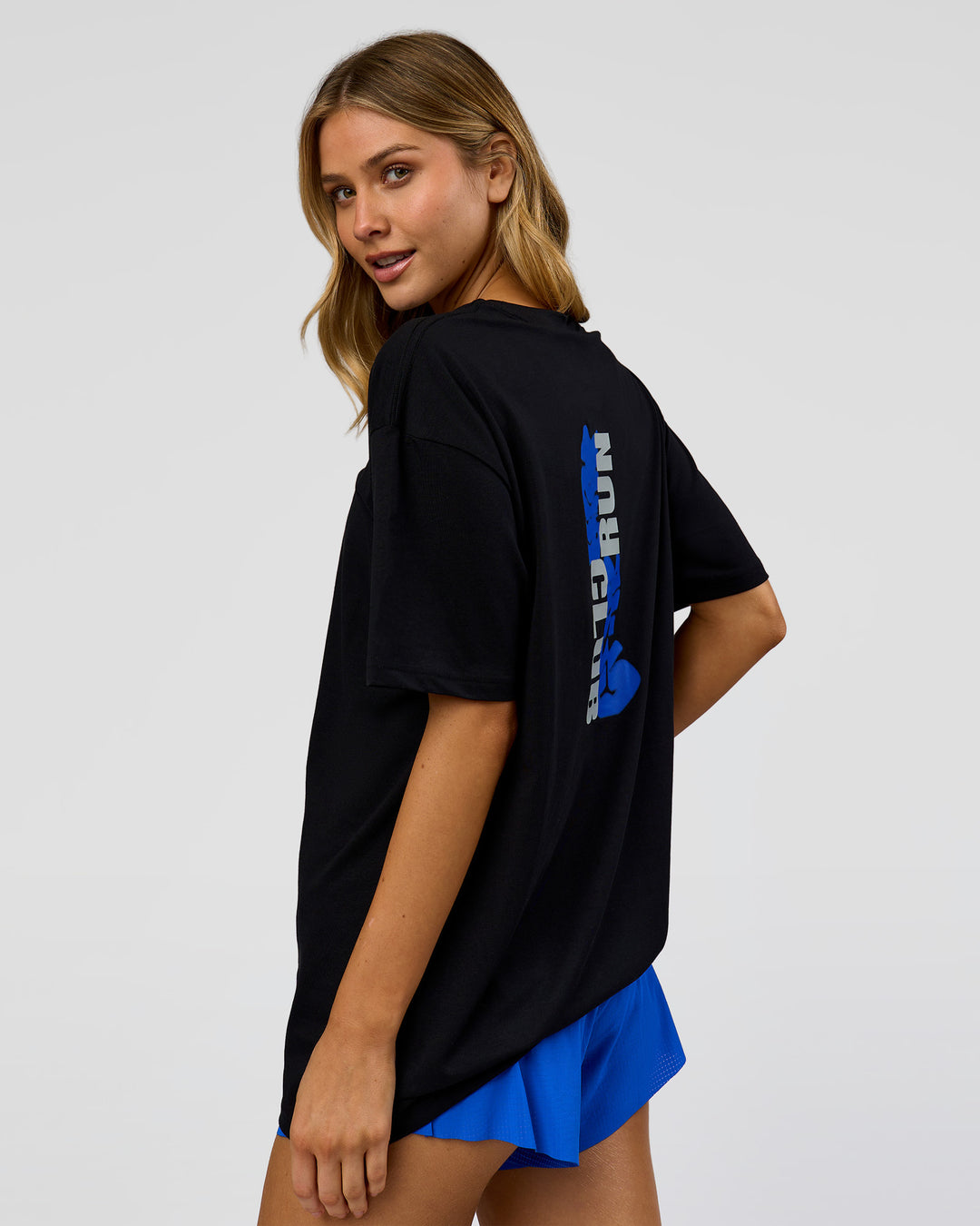 Woman wearing Run Club Elevate FLXCotton Oversized Tee - Black-Electric Indigo | Model:Leilani | Size:XS - view 11